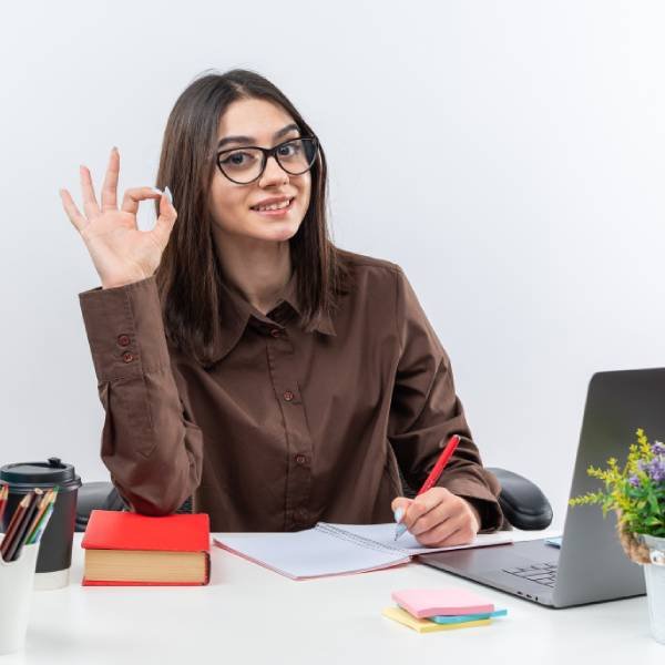 Smiling young school woman wearing glasses sits at table